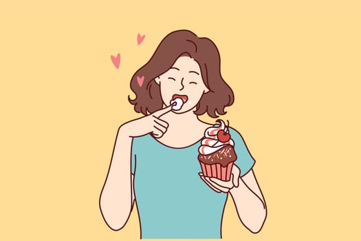 Woman eats delicious cupcake, licking sweet cream from finger and enjoying appetizing dessert bought in craft bakery. Beautiful girl having lunch with cupcake with fresh berries from cake shop