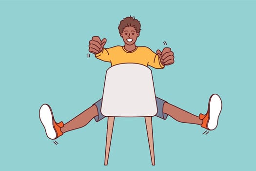 Man sitting on chair holds invisible car steering wheel in hands and imagines that is driving on high-speed road working as taxi driver. African american teenager guy drives invisible car