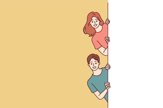 Happy man and woman with white banner peeking out recommending to pay attention to good advertisement offer. Young couple of guy and girl holding billboard for commercial or discount advertisement
