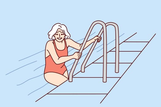 Elderly woman in pool of hotel or spa after finishing aqua treatments for healthy lifestyle. Retired woman in swimming suit in pool leaves water completing workout and wellness fitness session