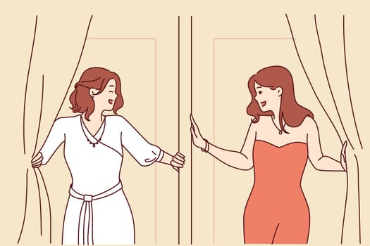 Two women leave fitting room in elegant evening dresses for gala dinner or party. Attractive girls in beautiful dresses are standing near fitting room of fashionable clothes store for festive ball