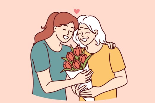Woman hugs elderly mother and gives bouquet of flowers congratulating with birthday or mother day and thanks for good upbringing. Grown up daughter takes care of mother of retirement age