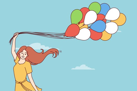 Happy young woman with balloons rejoices at onset of spring and warm weather standing on background of blue sky. Cheerful girl in summer dress with balloons symbolizing lightness and good mood