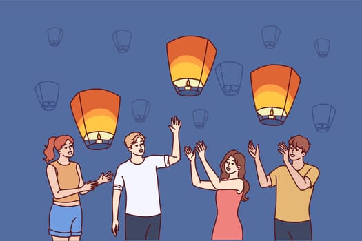 Group of people launch aerial chinese lanterns while making cherished wishes during traditional festival. Young friendly men and women with air lanterns celebrate chinese new year.