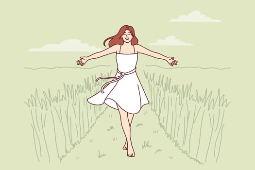 Woman walks along path among tall grass enjoying beautiful nature in rural or farming area. Girl in dress enjoys walk in wild nature or agricultural field in ecologically clean place.