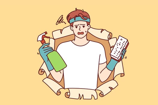 Disgruntled man with cleaning brush and bottle filled with chemical detergent that removes grease stains or dirt from furniture. Guy in casual clothes uses cleaning spray to do housework.