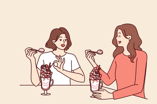 Women having lunch sitting in restaurant eating milkshake and discussing personal lives or plans for weekend. Girlfriends eat ice cream or milkshake in cafe wanting to cool off in hot summer weather