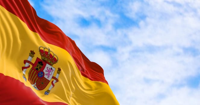The national flag of Spain waving in the wind in a clear day. European country. Three horizontal stripes in red, yellow, red, coat of arms on the left. 3d illustration render. Rippled textile.