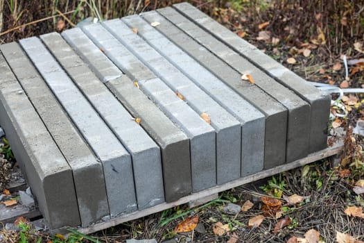 Borders for road repair. Building blocks are stacked. Concrete elements for the construction of a pedestrian zone. Gray stones on a green background.