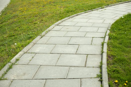 Path in park. Tile trail through park. Details of pedestrian zone. Place for walking. Tiles made of stone.