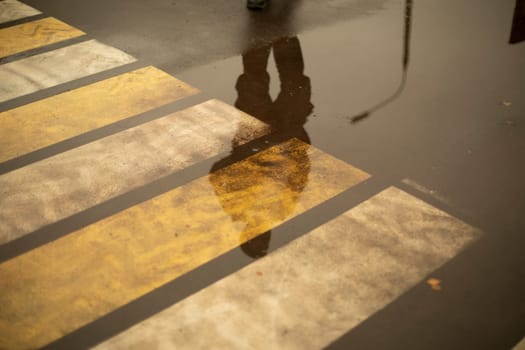 Pedestrian crossing across road in rain. Road markings for pedestrians. Strips in row on asphalt. Paint on road.