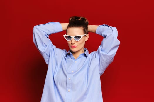 Portrait of playful adult woman in sunglasses holding hands behind head