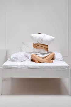 Cheerful woman hugs pillow sitting at the edge of the bed