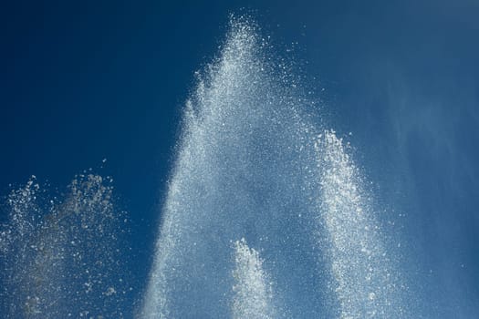 Jets of water against sky. Fountain in city. Details of fountain on street. Splash drops.