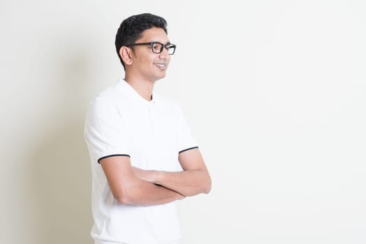 Portrait of happy Indian guy arms crossed looking at side. Asian man standing on plain background with shadow and copy space. Handsome male model.
