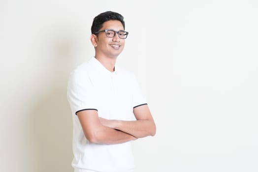 Portrait of happy Indian guy arms crossed looking at camera. Asian man standing on plain background with shadow and copy space. Handsome male model.