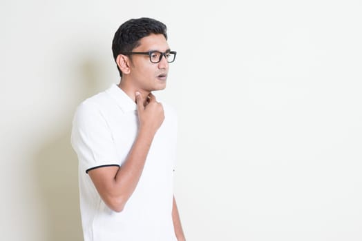 Portrait of Indian guy sore throat, hand on neck clearing throat. Asian man standing on plain background with shadow and copy space. Handsome male model.