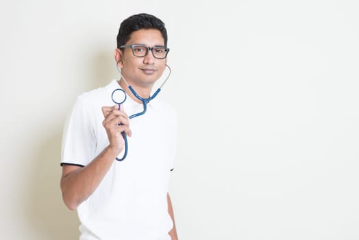 Indian medical student with stethoscope in hand. Asian man standing on plain background with shadow and copy space. Handsome male model.