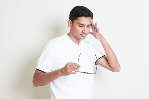 Portrait of tired Indian guy headache and massage his head. Asian man standing on plain background with shadow and copy space. Handsome male model.