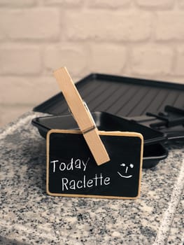 Small chalkboard with the inscription Today Raclette on a Raclette grill with space for text