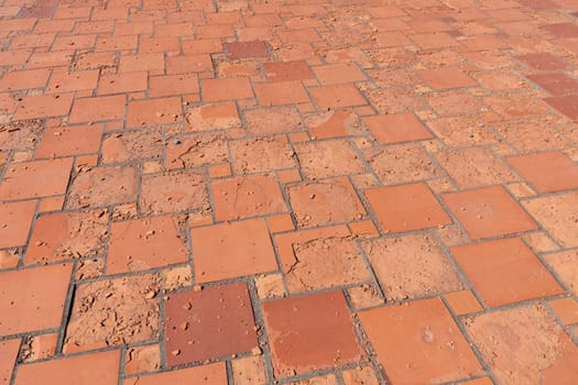 Red square floor tiles damaged by weathering or material defects. The surface is crumbling and the plates are disintegrating.