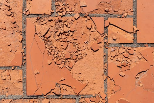 Red square floor tiles damaged by weathering or material defects. The surface is crumbling and the plates are disintegrating.