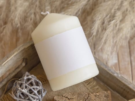 Candle with blank paper label on wooden tray with dried pampas grass, Close up, copy space. Boho packaging mock up. Home decorations, Bohemian or scandinavian style..