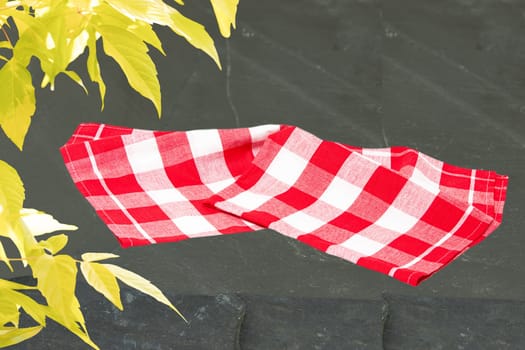 Empty red checkered tablecloth or napkin and yellow maple in spring on slate plate. Space for your food and product display montage. Recipe concept.