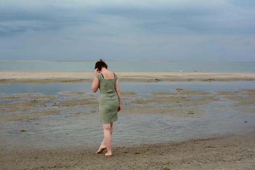 Young woman in a short green dress is standing in front of the sea on a sandy beach