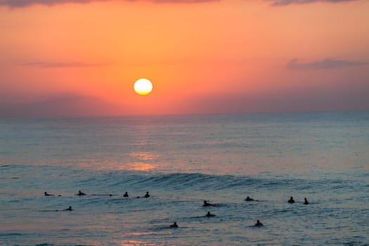 Surfing surfers in ocean wave waters early dawn sunrise on the horizon.