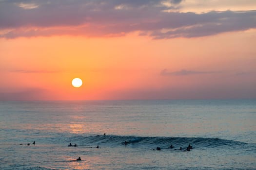 Surfing surfers in ocean wave waters early dawn sunrise on the horizon.