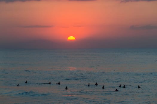 Surfing surfers in ocean wave waters early dawn sunrise on the horizon.