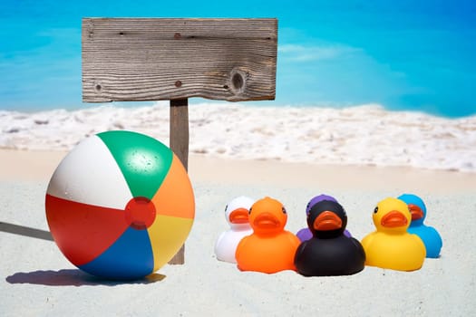 Six colorful rubber ducks and a wooden sign on the beach