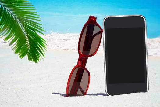 Black smartphone,sunglasses under palm fronds on the beach
