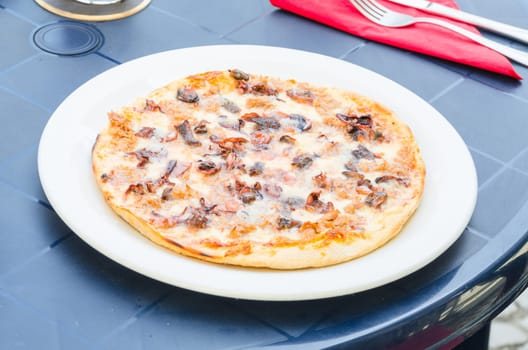 Seafood pizza on a simple blue table outside a pizzeria.