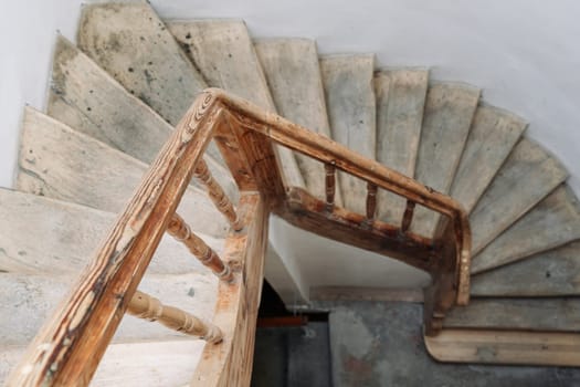 The steps of a wooden spiral staircase in an old building. An old wooden staircase in an old building with white walls.