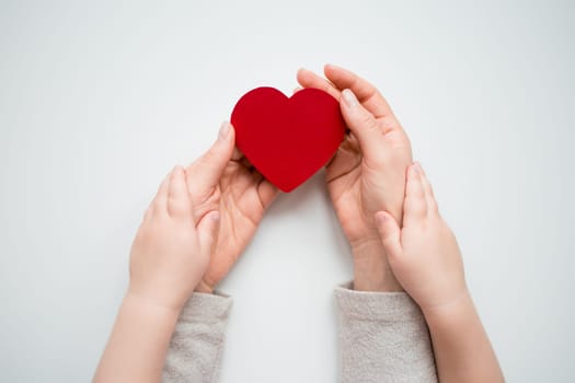 Adult and child holding red heart symbolizing love and care.