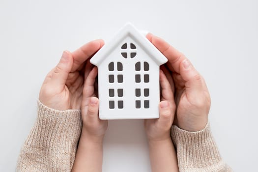Caucasian hands holding ceramic house model representing home safety and security.