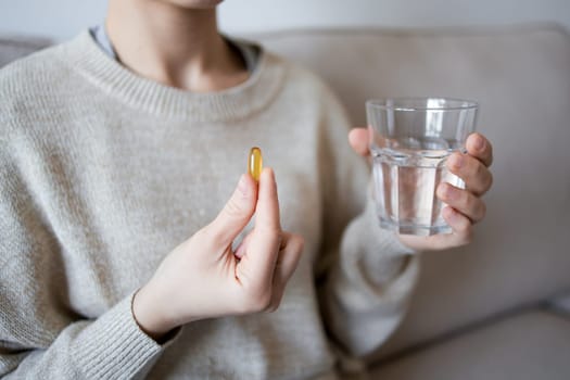 Female taking fish oil capsule with water in cozy home setting.