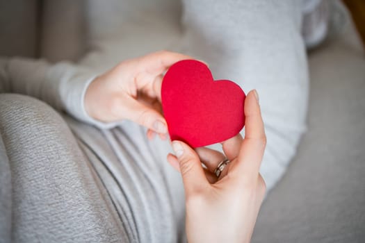 Pregnant woman holding red heart symbolizing love and connection.