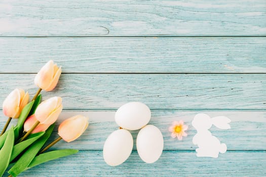 Happy Easter Day Concept. Top view of holiday banner background design white easter eggs and spring tulip flowers on blue wooden background with empty copy space, celebration greeting card