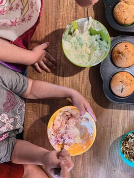 Group of children baking cupcakes, preparing ingredients, toppings, sprinkles for decorating cookies. Kids learning to cook, working together in kitchen at home. Concept of happy family