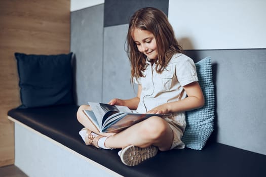 Schoolgirl reading book in school library. Primary school pupil is involved in book. Child doing homework. Smart girl learning from book. Benefits of everyday reading. Child curiosity