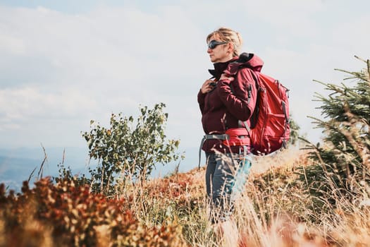 Woman with backpack hiking in mountains, spending summer vacation close to nature. Woman walking on path among bushes and grass