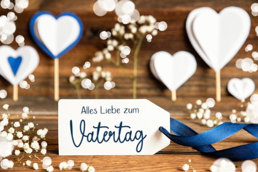 Label With German Text Alles Liebe Zum Vatertag Means Happy Fathers Day. White Festive And Atmospheric Decoration Like Hearts, Flowers And A Blue Bow. Vintage, Wooden Background.