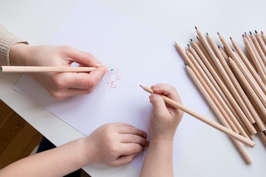 Child and adult drawing together with colored pencils on white paper.