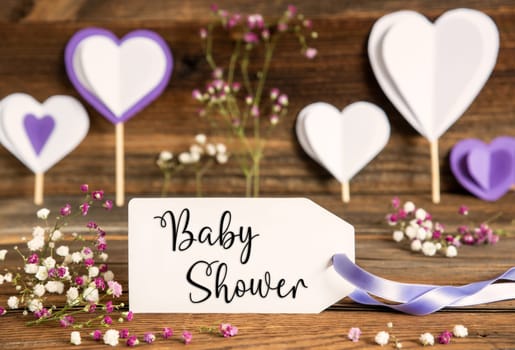 Label With English Text Baby Shower. Purple And Lilac Decoration And Spring Flower Arrangement. Heart Symbols With Wooden Background.