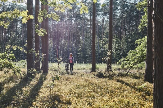 Active woman cycling on forest road. Female riding bicycle off-road route on summer vacation day. Woman wearing bicycle helmet and gloves