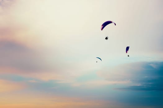 Paragliders flying in the sky. Paragliding in the cloudy colorful sky at sunset. Extreme activity, hobby and sport