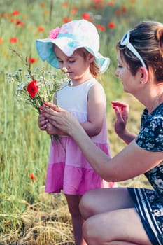 Mother and her little daughter in the field of wild flowers. Little girl picking the spring flowers for her mom for Mother's Day in the meadow. Nature scene, family time